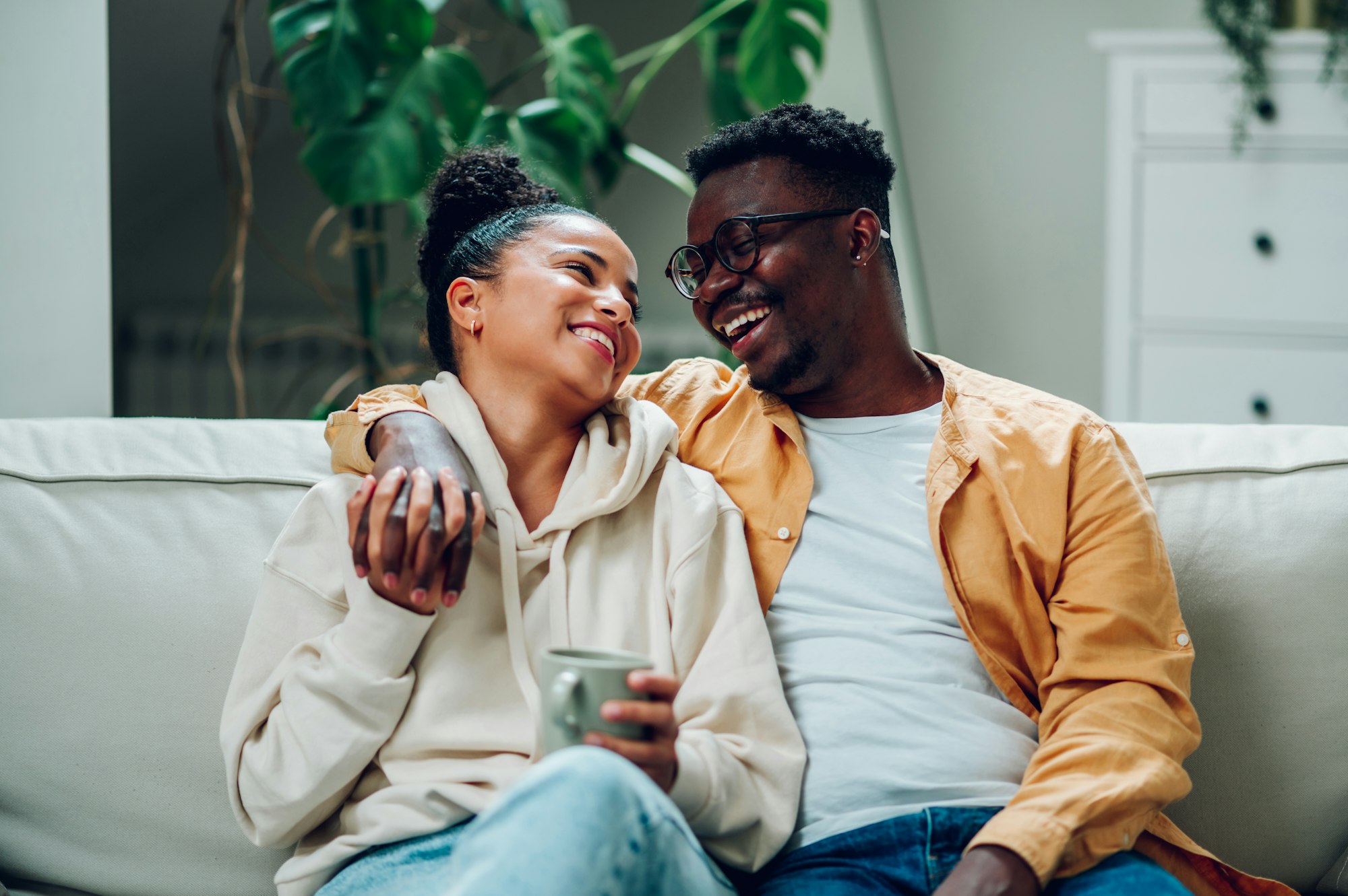 Multiracial couple relaxing on a couch at home and drinking coffee