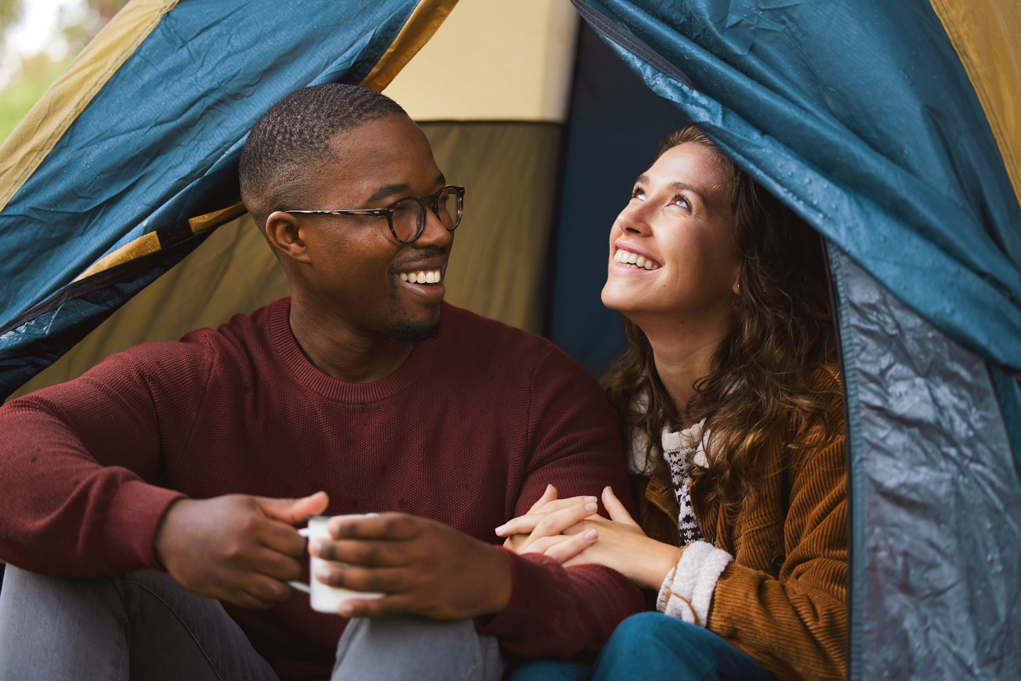 Shot of a young couple drinking coffee while sitting in their tent